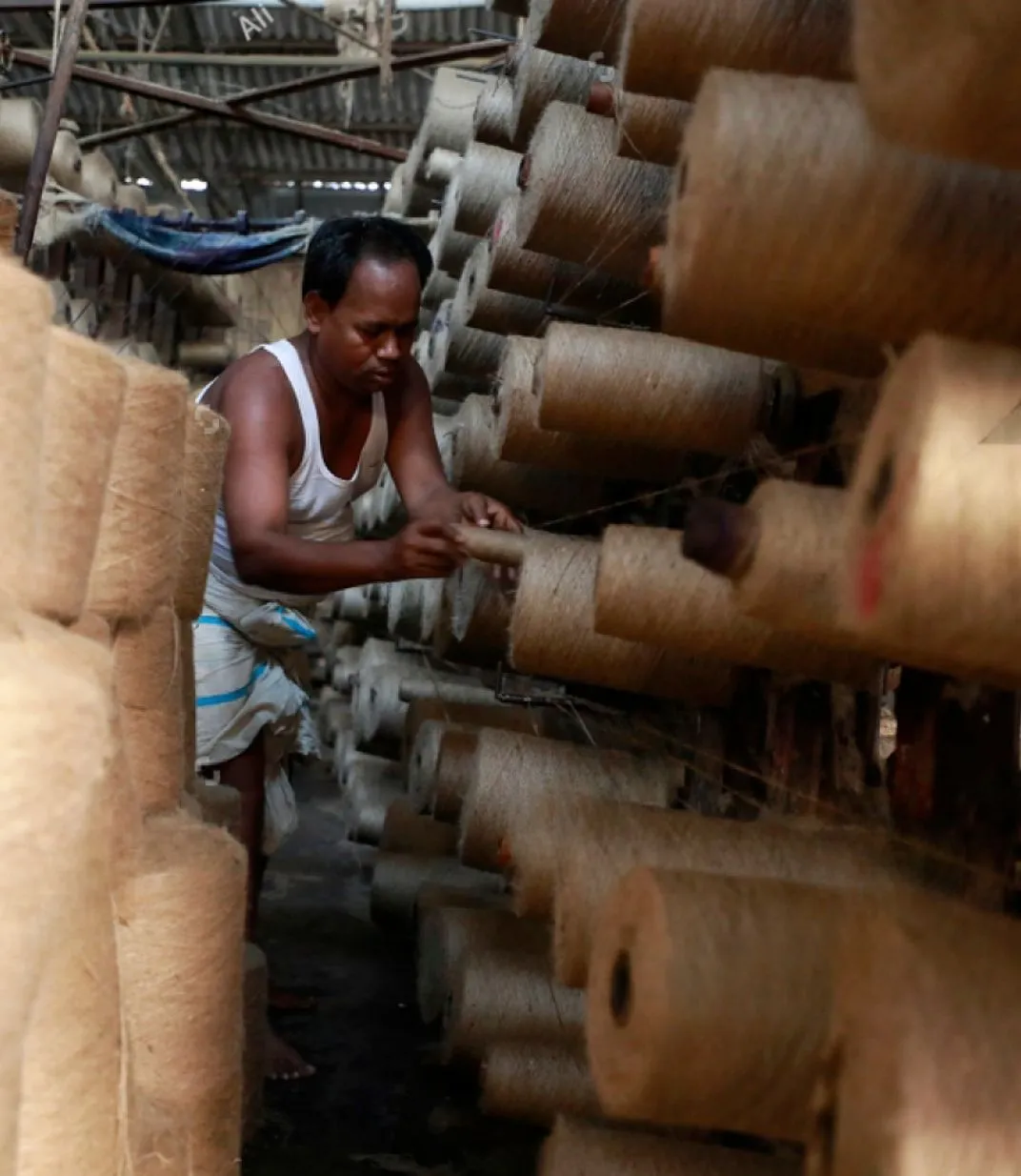 Workers operating jute yarn spinning machine in factory.