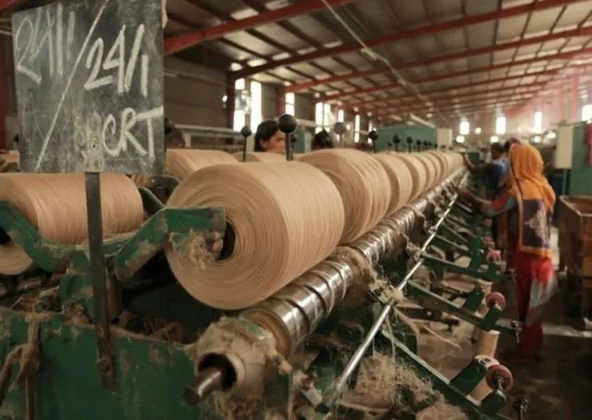 Workers operating jute yarn spinning machine in factory.